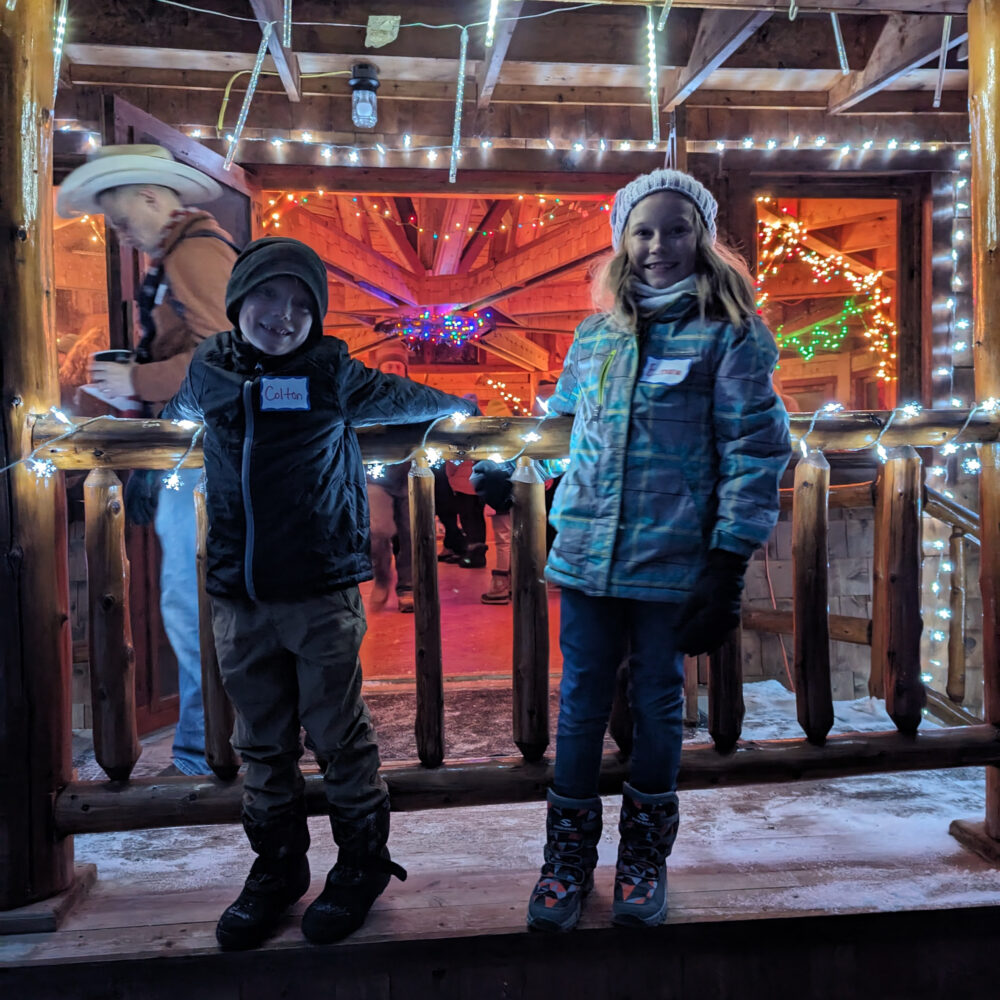 Two kids in front of the Redwood Hill Preserve lit up with Christmas lights