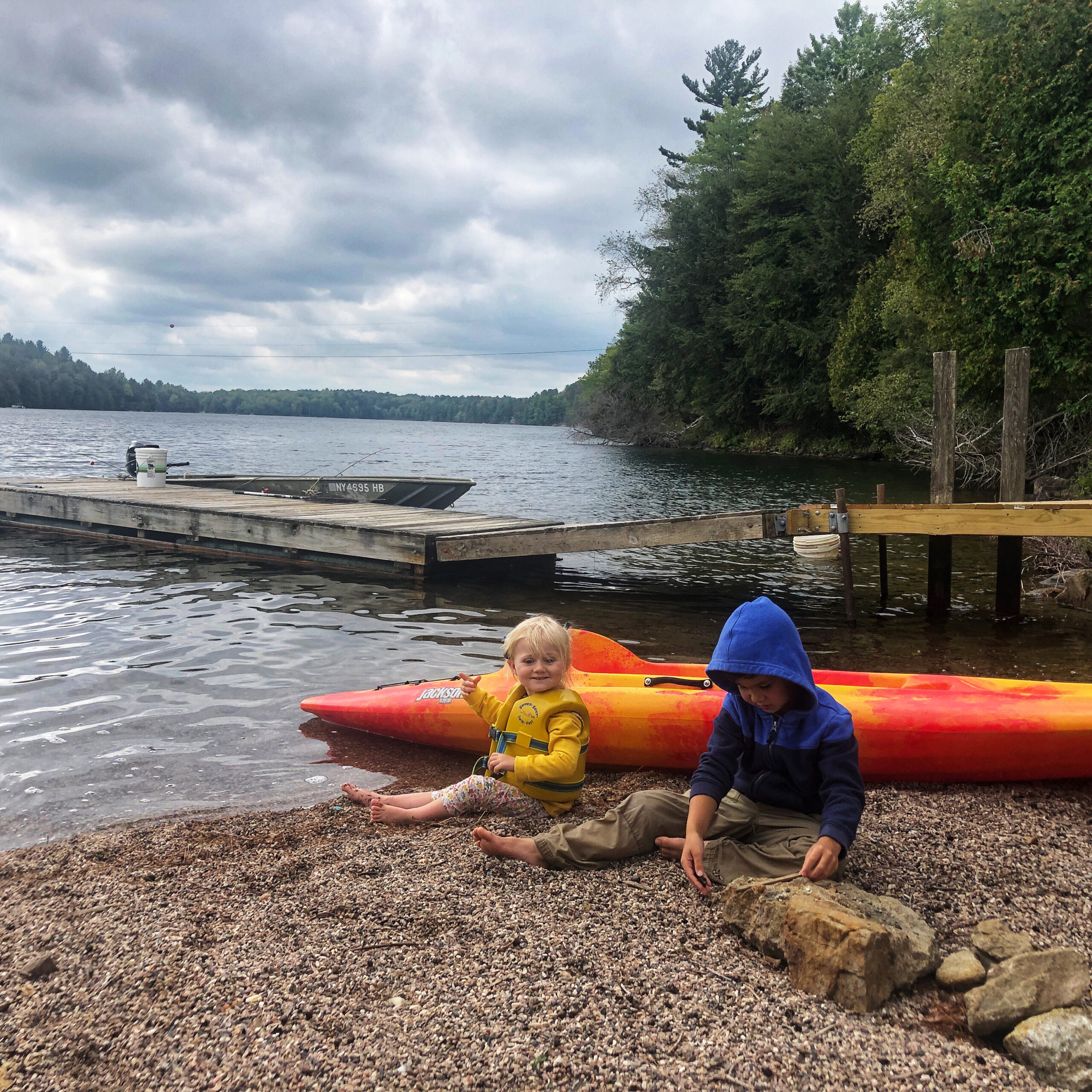 two kids sitting lakeside in front of kayaks